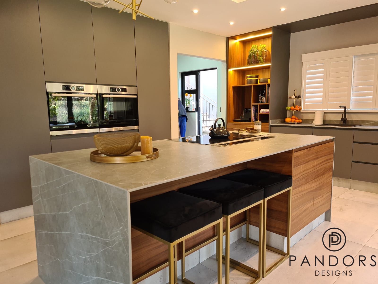 Bespoke Pandors Designs kitchen with a marble waterfall island, walnut cabinetry and brass-framed bar stools