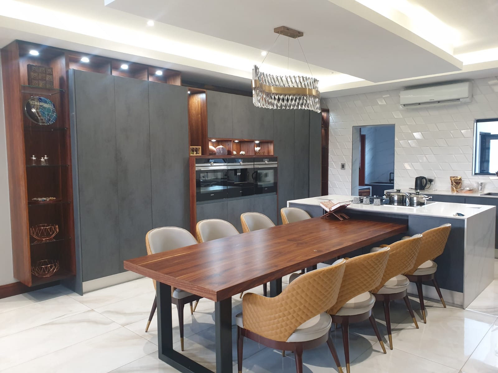 Open-plan Pandors Designs kitchen with charcoal cabinetry, a live-edge walnut dining table and a statement chandelier