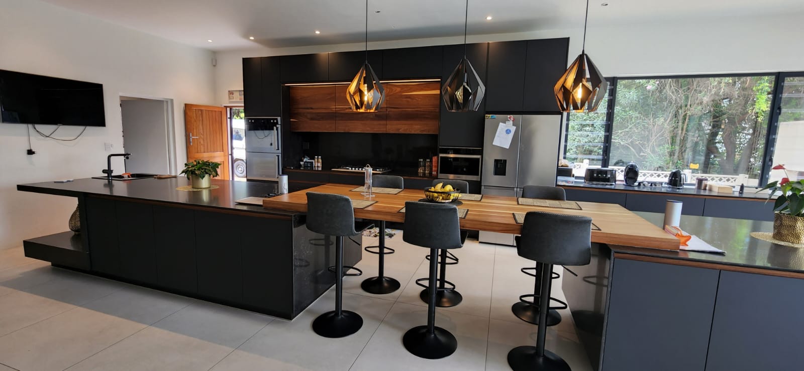 Bold architectural Pandors Designs kitchen in matte black cabinetry with walnut accents and geometric pendant lights