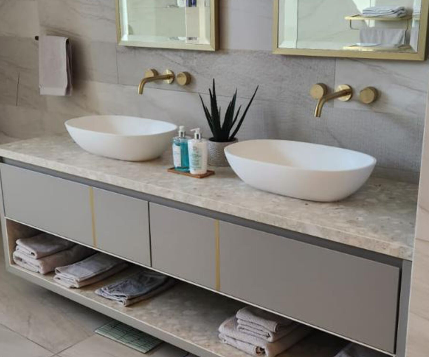 Pandors Designs bathroom vanity in soft grey cabinetry with a stone countertop, brass fittings and folded towels