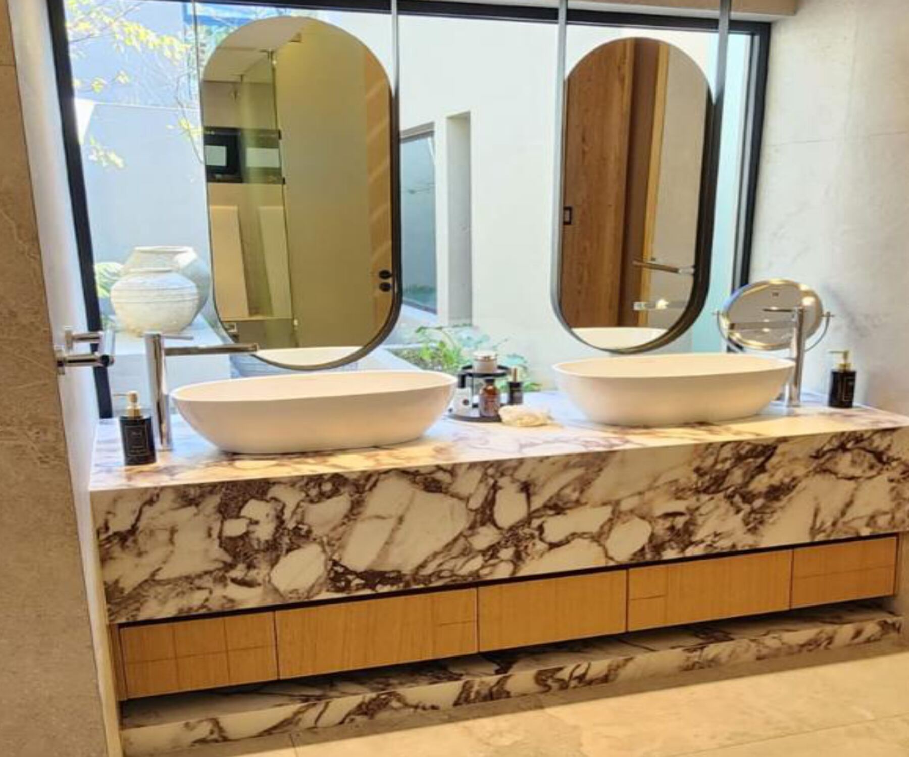 Pandors Designs bathroom vanity in warm oak cabinetry with a Calacatta Viola marble countertop and backlit oval mirrors