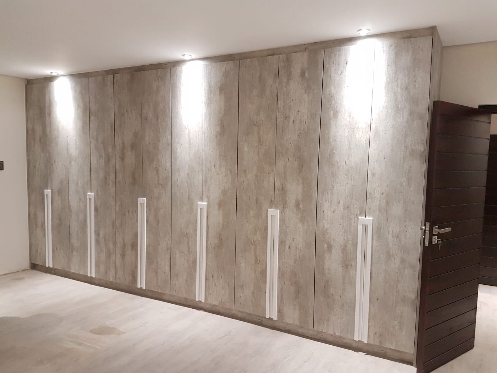 Full-width Pandors Designs built-in wardrobe wall in a concrete-look finish with slim vertical handles