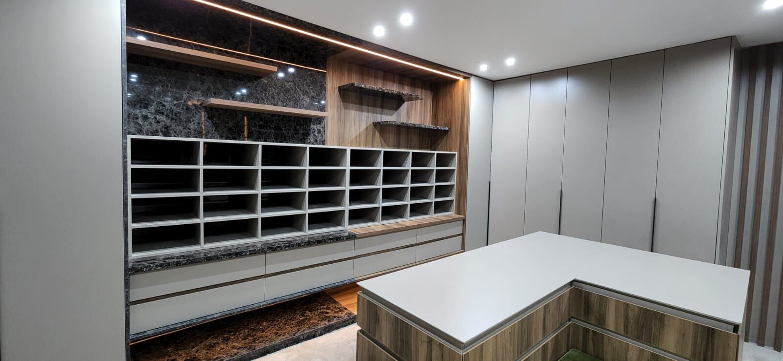 Pandors Designs walk-in closet with pigeonhole shoe storage, marble-effect shelving and a wood-finish drawer island